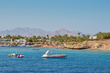 Fototapeta na wymiar speedboat off the coast, sea, beach, vacationers, buildings, against the backdrop of mountains and sky, Red Sea, Egypt
