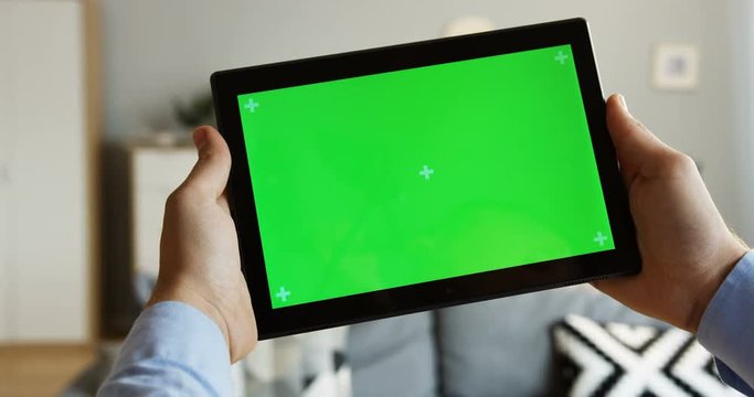 Close up of the male hands holding a black tablet computer horizontally with a green screen and tracking motion. At home. Chroma key. Inside