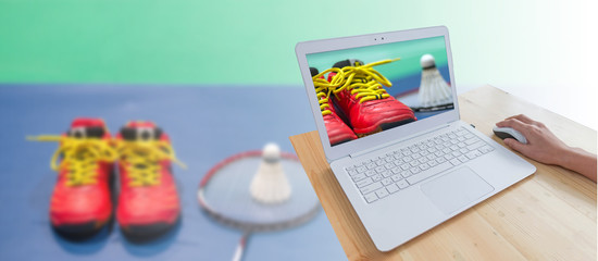Badminton sport background, closeup badminton red shoes with blurred shuttlecock and racket in screen laptop computer and hand using mouse on wood table isolated on blurred badminton shuttlecock