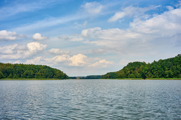 Summer landscape with forest lake under a blue cloudy sky. Kuyavian-Pomeranian, Poland