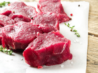Pieces of raw meat. Raw beef with spices and thyme on wooden rough rustic background, side view, close-up.