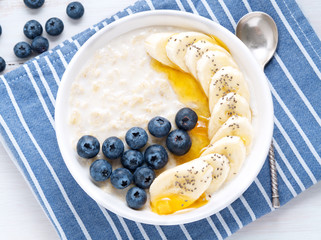 Oatmeal with bananas, blueberries, chia, jam, honey, blue napkin on white wooden background. Close-up. Top view