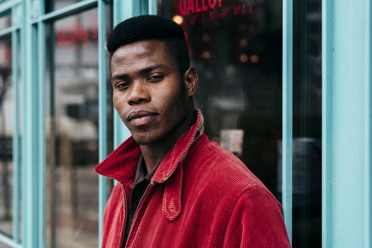 Young black man in red jacket standing by cafe