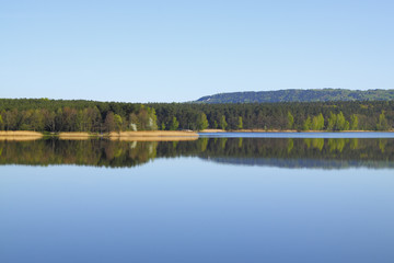 Fototapeta premium Lake with forest line mirrored in calm water surface
