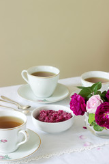 Jam from the petals of the Damascus rose, a cup of green tea and a vase of roses on a light table....