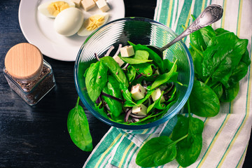 Salad with fresh spinach leaves, cheese, red onion, flax seeds on a dark wooden table.