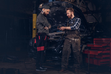 Obraz na płótnie Canvas Two mechanics talking during repairs a broken car in a garage.