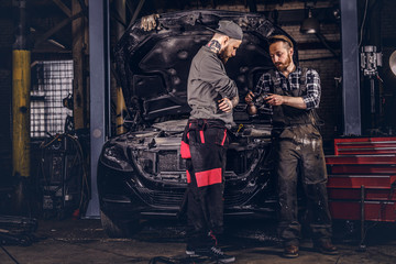 Two mechanics talking during repairs a broken car in a garage.