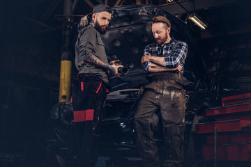 Obraz na płótnie Canvas Two mechanic talking during repairs a broken car in a garage.