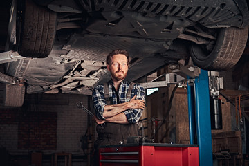 Mechanic crossed hands while standing under lifting car in a repair garage.