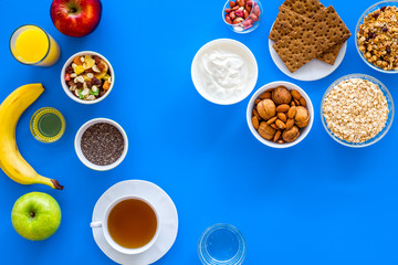 Make a menu for wholesome breakfast. Fruits, oatmeal, yogurt, nuts, crispbreads, chia on blue background top view copy space