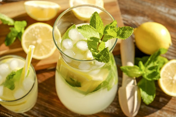Iced lemonade pitcher, wooden juicer & one glass of cold citrus beverage with lemon slices, mint...