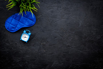 Healthy sleep concept. Sleeping mask near alarm clock on black background top view copy space