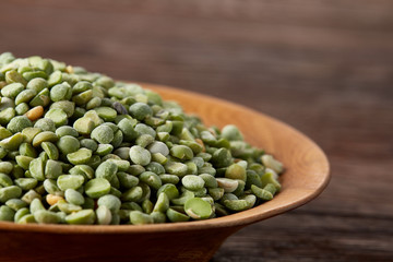 Raw green peas on a wooden plate over rustic background, close-up, selective focus, shallow depth of field.