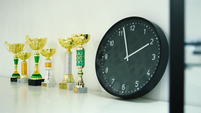 Trophy award for the winner show on shelf. Stock. Clock and trophies on the shelf. The concept of time and sports