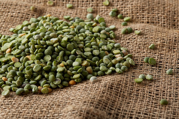 Pile of green peas on burlap tablecloth, close-up, top view, selective focus.