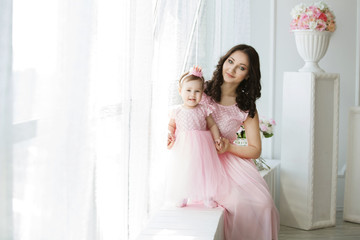 Fototapeta na wymiar happy mother and one-year-old child girl in pink dresses on birthday party.