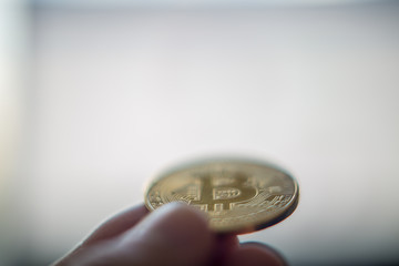 Hand holding Bitcoin coin offering to computer screen with store site on screen. Concept of virtual purchase with Bitcoin coin