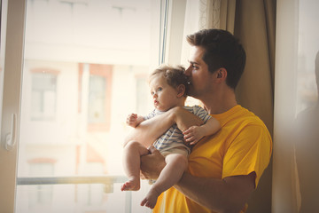 Young brunet father in yellow shirt playing with a little baby at home.