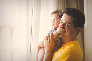 Young brunet father in yellow shirt playing with a little baby at home.