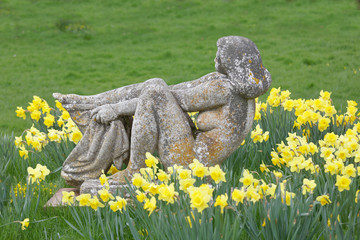 Stone statue of a naked woman with a towel and lots of daffodil flowers in the city Borgholm on the island Oland, Sweden