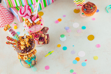 Two freak shakes with donuts and caramel popcorn on the party table with copy space