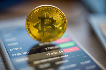 Metal Bitcoin coins and mobile screen showing quotation of the day Bitcoin - modern virtual