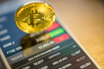 Metal Bitcoin coins and mobile screen showing quotation of the day Bitcoin - modern virtual