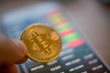 Metal Bitcoin coins and mobile screen showing quotation of the day Bitcoin - modern virtual