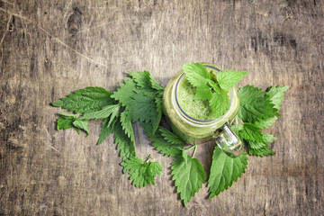 Obraz na płótnie Canvas Fresh green smoothie with wild nettle and other herbs in mason jar on rustic wooden background.