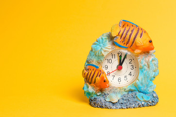 Fototapeta premium a clock with fish on a yellow background, a place for text. summer time. arrow points to the beginning of the first. alarm clock