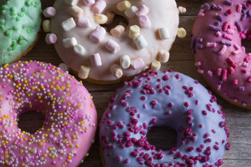 Assortment of colorful frosted doughnuts. Glazed sprinkles with marshmallow and chocolate on wooden background. Top view, close up.