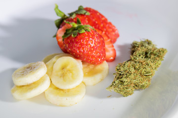Trimmed marijuana bud with fresh strawberries and bananas on white