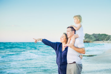 Happy family- pregnant mother, father and daughter embracing each other and watching ahead to the sea during walk on the beach. Relax by the calm sea in sunshine. Family vacation. Selective focus.