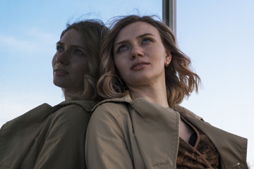 Attractive Young Blonde Woman in Trench walking in City Mirrors with Vintage Suitcase