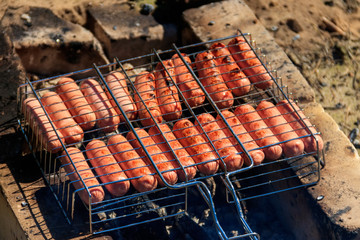 Grilling sausages in barbecue grill cooking on campfire