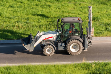 Tractor excavator with a bucket from the front behind, driving along the highway