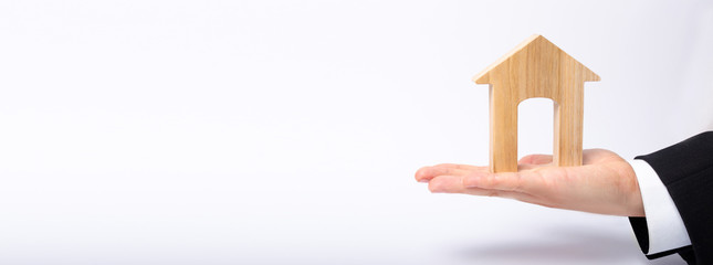 The businessman's hand stretches a wooden house with a large doorway. The concept of commercial real estate, the purchase and sale of residential buildings, apartments. Rental of property. Banner