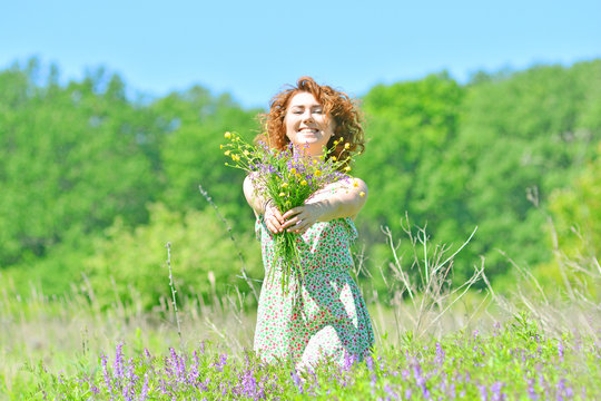 Girl in a meadow holds out a bouquet to the viewer. Summer background with a beautiful cheerfull girl with bouquet of flowers.