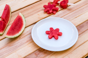 sliced ​​watermelon and a piece of watermelon shaped like a flower on a white plate on wooden table