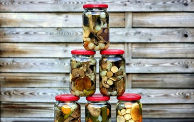 Delicious food, kitchen and homemade concept: forest mushrooms in jars on a wooden background.