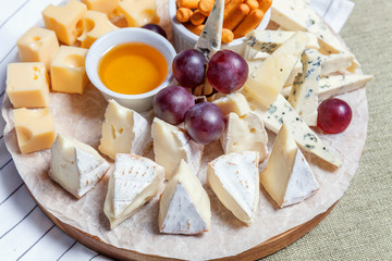 Board with different types of cheese: Dor blu, chedar, Parmesan, brie, honey sauce, finger bread and grape. Restaurant menu plate