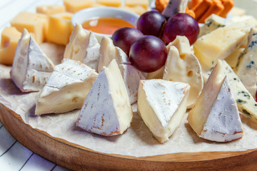 Board with different types of cheese: Dor blu, chedar, Parmesan, brie, honey sauce, finger bread and grape. Restaurant menu plate