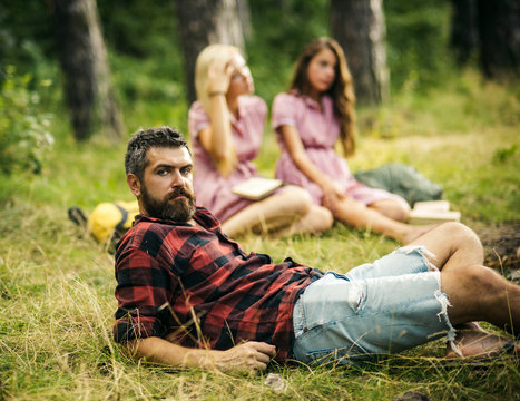 Bearded man in lumberjack shirt spending time with friends outdoors. Handsome man lying on glass in woods. Outdoor recreation and nature concepts