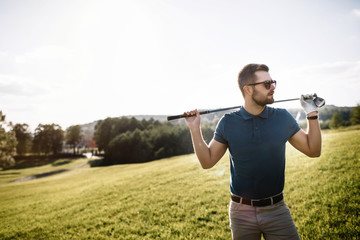 portrait of stylish golfer in glasses standing on golf course wi