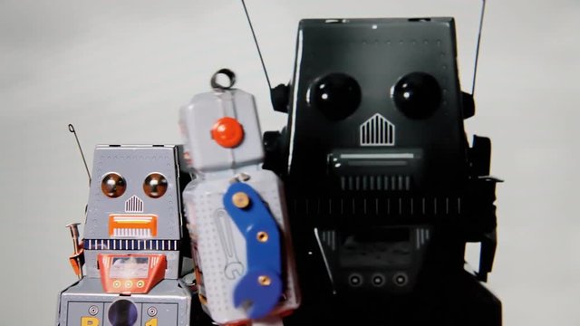 A war between two tin toy robots clashing into each other, over a background of ominous black shapes and clouds.
