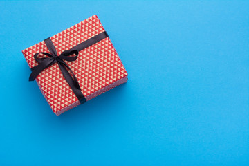 Hands holding wrapped gift box with colored ribbon as a present for Christmas, new year, mother's day, anniversary, birthday, party,  on blue background, top view. Present for a colleague at work.