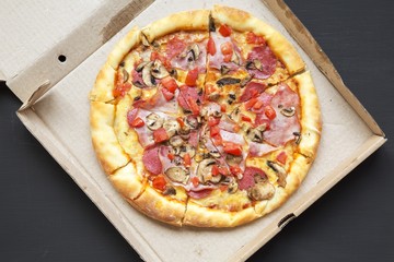 Top view, freshly baked pizza in a cardboard box on dark background. From above, flat lay.