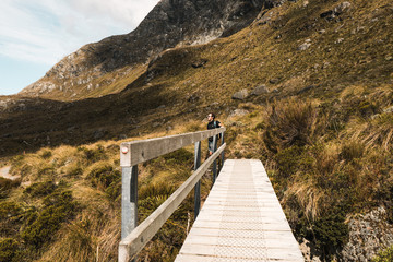 Fototapeta na wymiar New Zealand, Routeburn track: photo of young man near wooden bridge in mountains 