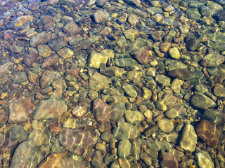 Clear water of a mountain river. Sun glare on river stones under clear water